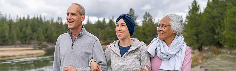adult person with cancer walking outdoors arm in arm with her parents, all smiling