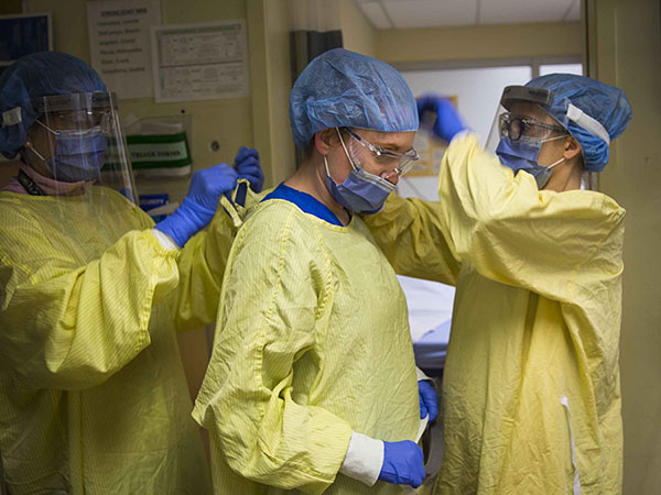Three nurses putting on PPE