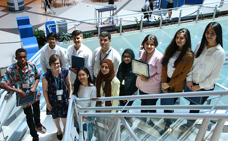 Group of Summer Student Clinician Scientist program graduates from 2019 cohort standing on staircase at Princess Margaret with Program Lead Sandra Clark