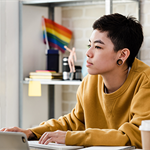 person on computer with pride flag in background
