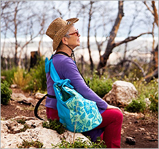 Woman in sunhat sitting outside on a rock near lake