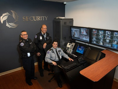 Image of three security guards in front of UHN Security sign, to the left of monitors 