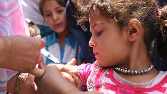 An afghan female health worker gives measles vaccine to a small girl