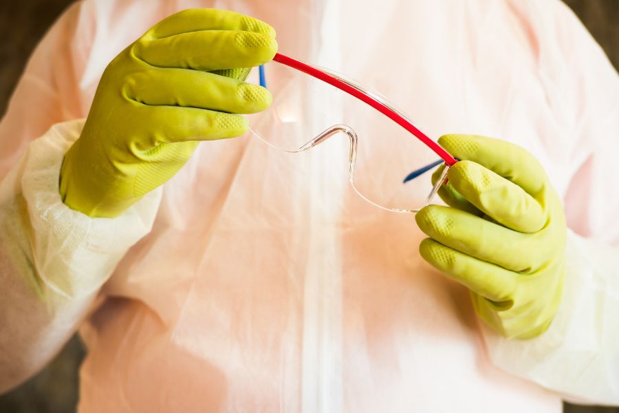 Person wearing a hazmat suit and holding safety goggles in their hands while wearing gloves