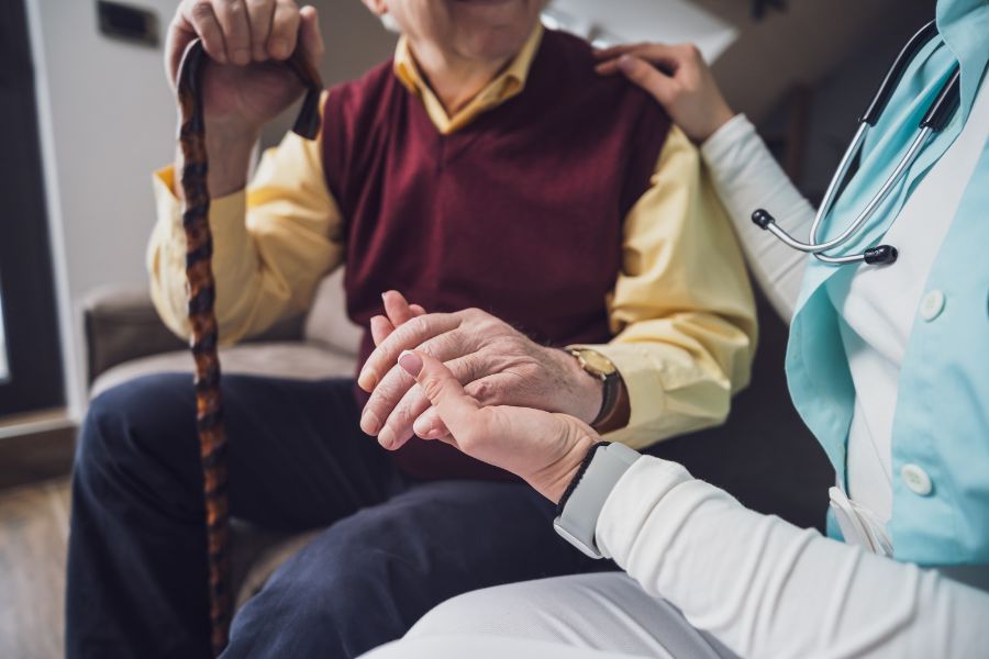an elderly man holding a cane in one and holding the hand of a healthcare worker with the other hand