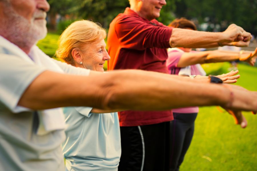 Seniors exercise together outdoors in the sunlight